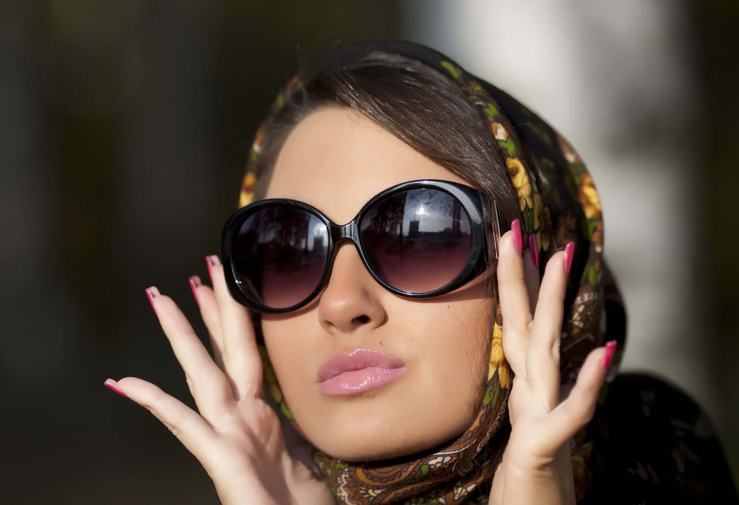 image montrant une femme avec une peau lisse, portant des lunettes de soleil et un foulard dans les cheveux.