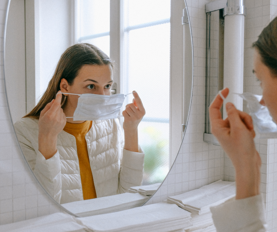 Femme qui met un masque chirurgical sur son visage devant un miroir